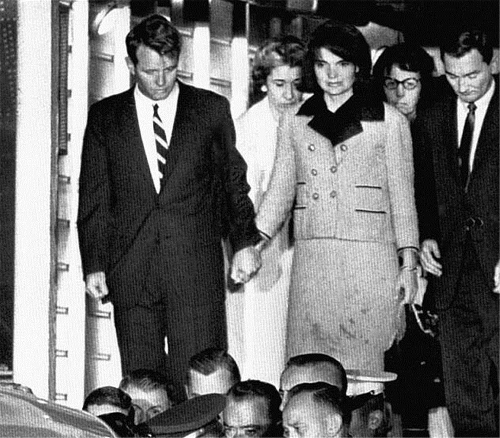 总统的亲弟弟罗伯特·肯尼迪牵着沾满血污的,粉色的杰奎琳回到住所
